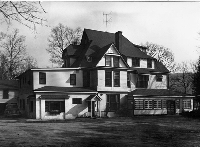Victorian-style house features multiple gables, a large porch, and a side garage. The image highlights its architectural details and surrounding trees.