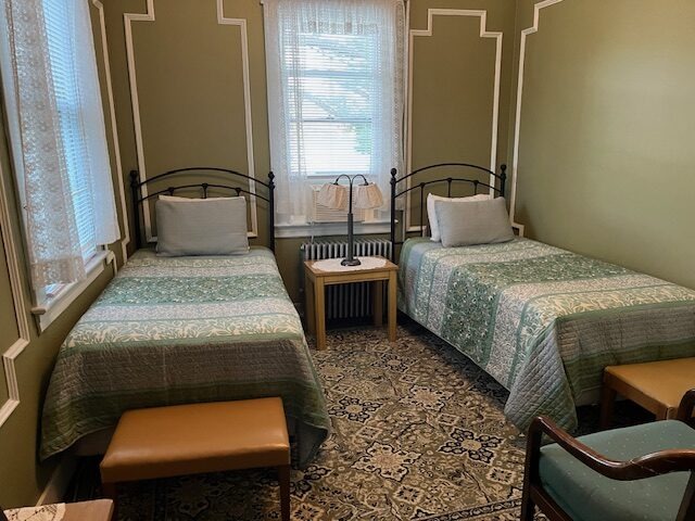 Cozy guest room featuring two twin beds with green patterned quilts, a small wooden table, and a decorative rug, ideal for a comfortable stay.