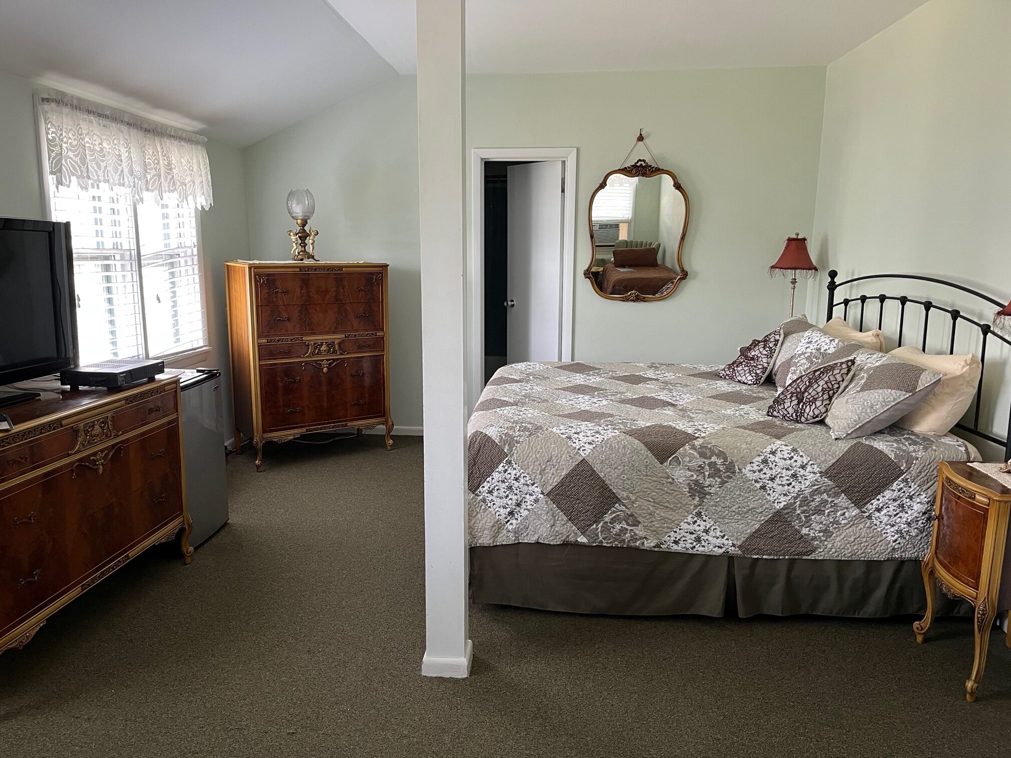 Cozy bedroom featuring a patterned quilted bed, vintage furniture, a TV, and a decorative mirror, creating a warm and inviting atmosphere.